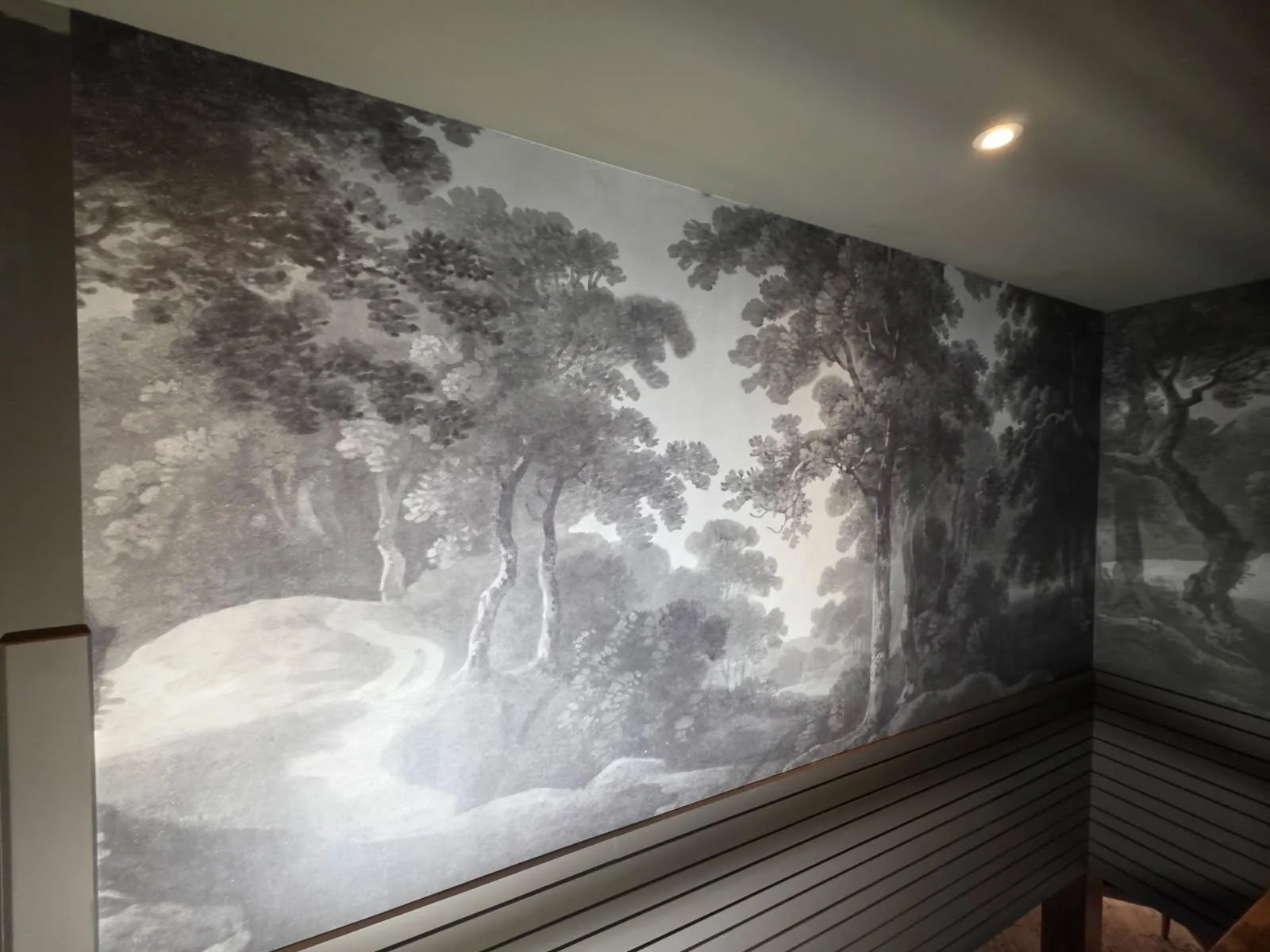 Grayscale forest mural wrapping an inside stairwell corner above horizontal slat paneling