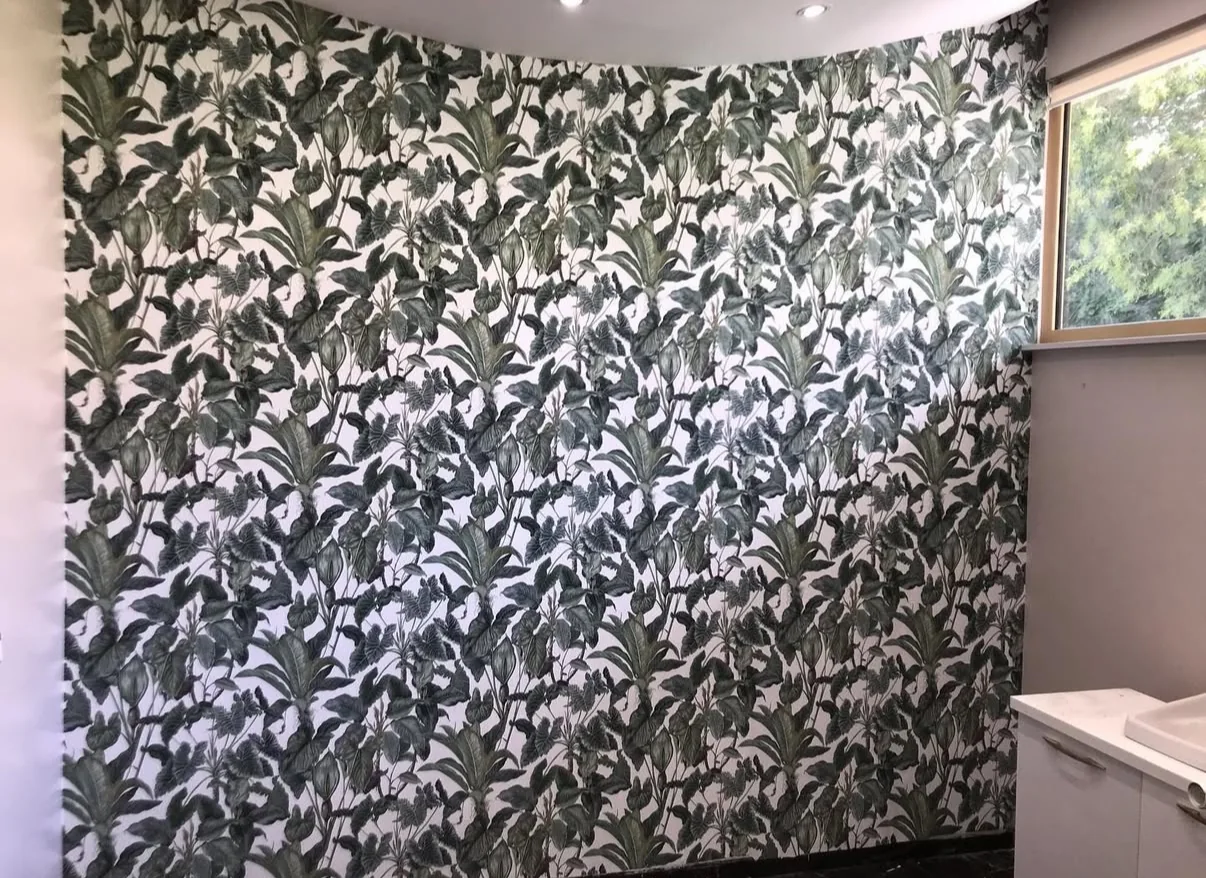 Finished powder room with dense charcoal and green botanical wallpaper beside a window and white vanity