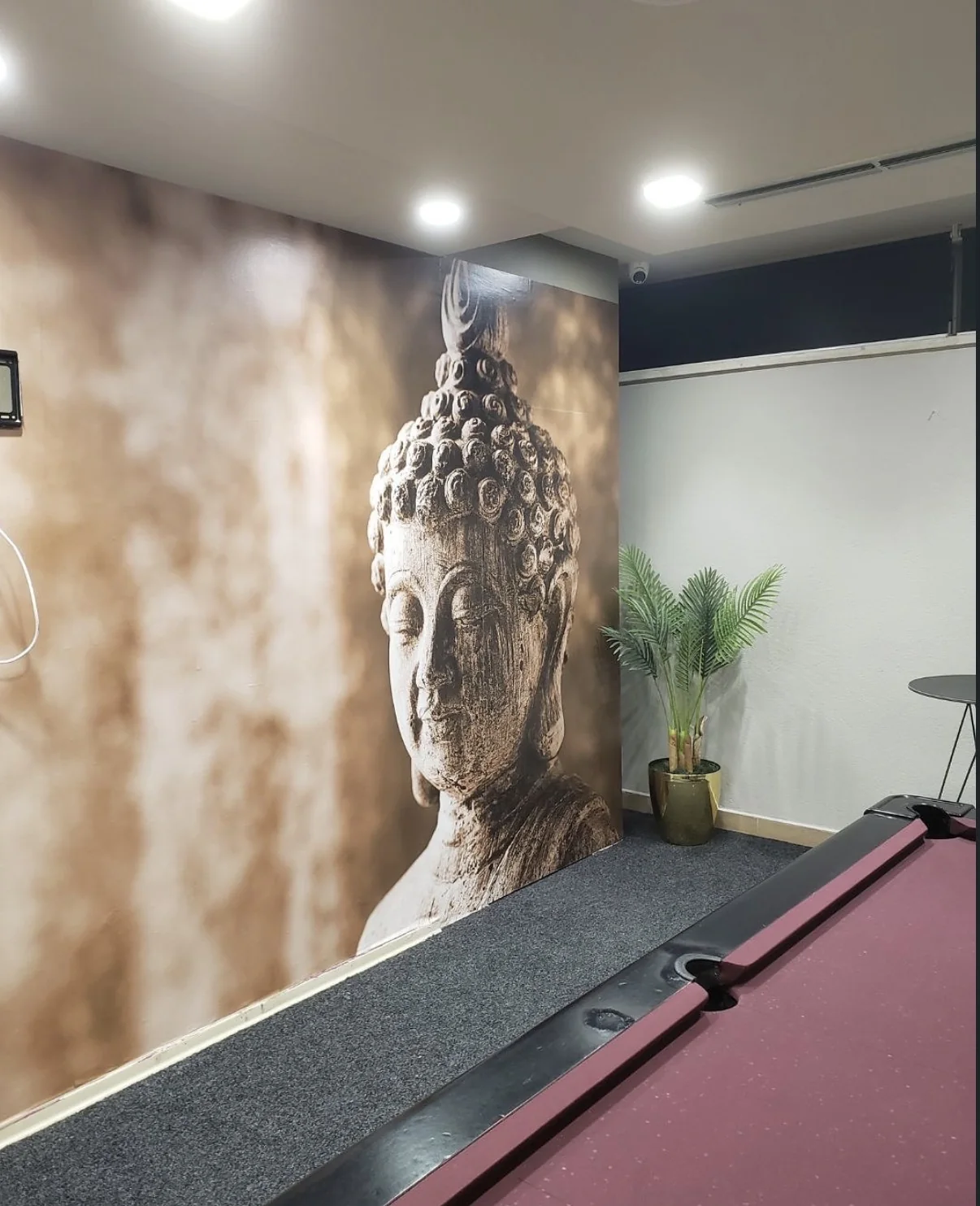 Large sepia Buddha-head mural installed on a feature wall beside a pool table in an entertainment room