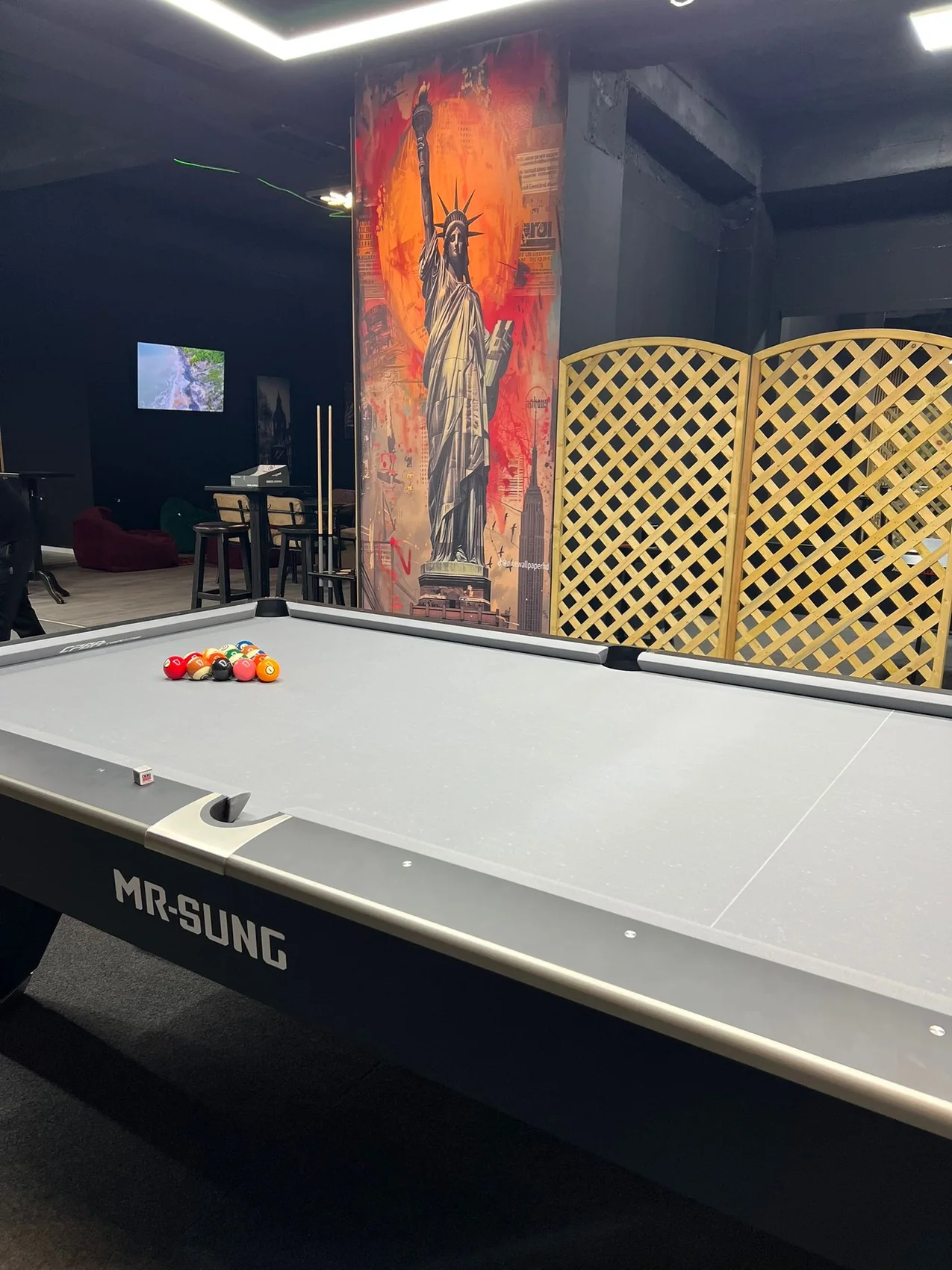 Orange and gray Statue of Liberty and New York mural installed beside a pool table in a dark entertainment room