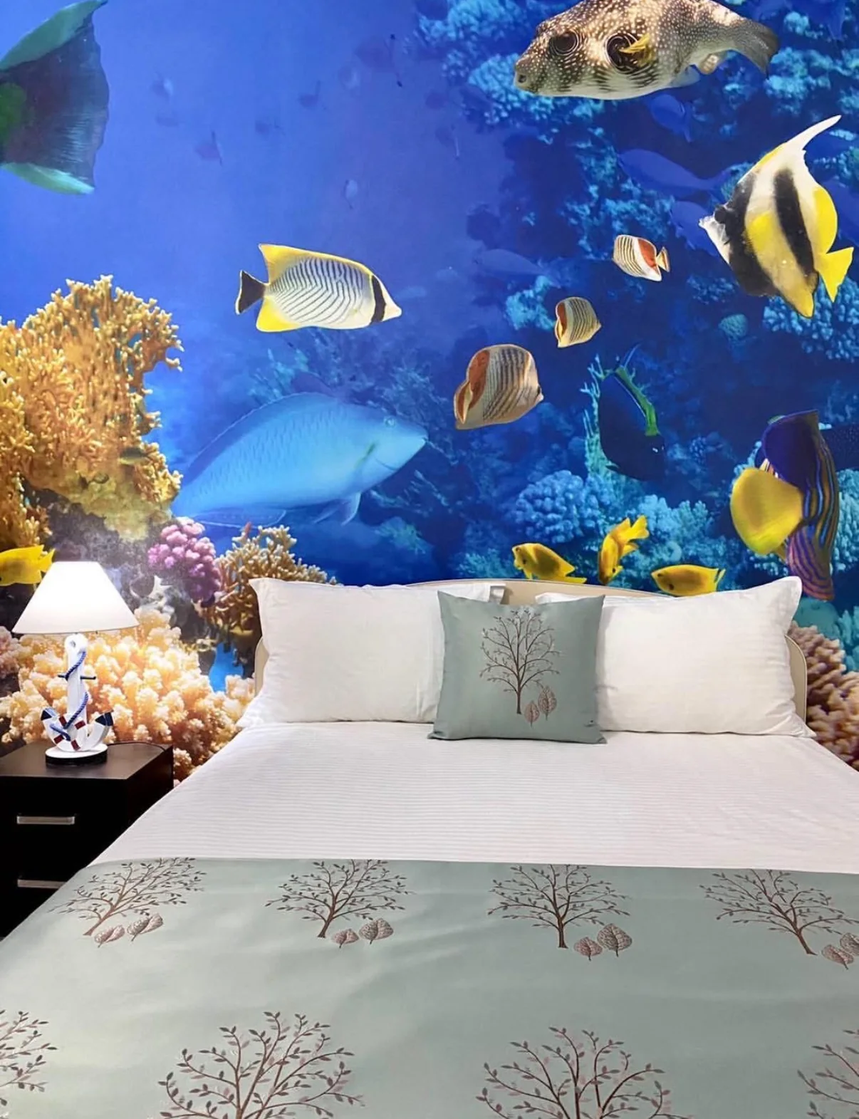 Finished bedroom with a deep blue underwater mural of tropical fish and coral behind a made bed