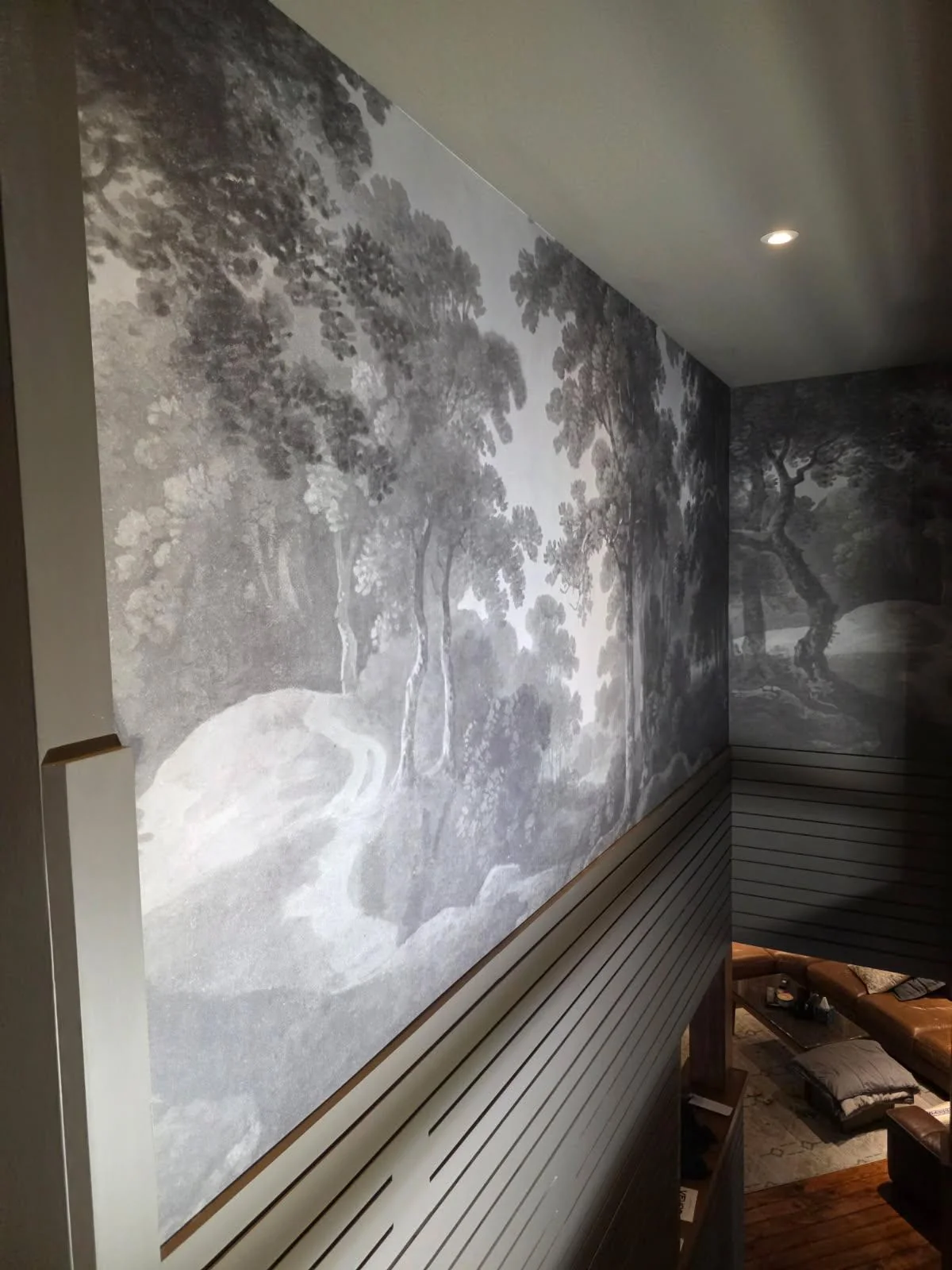 Monochrome woodland landscape mural installed above horizontal gray paneling on a residential stairwell