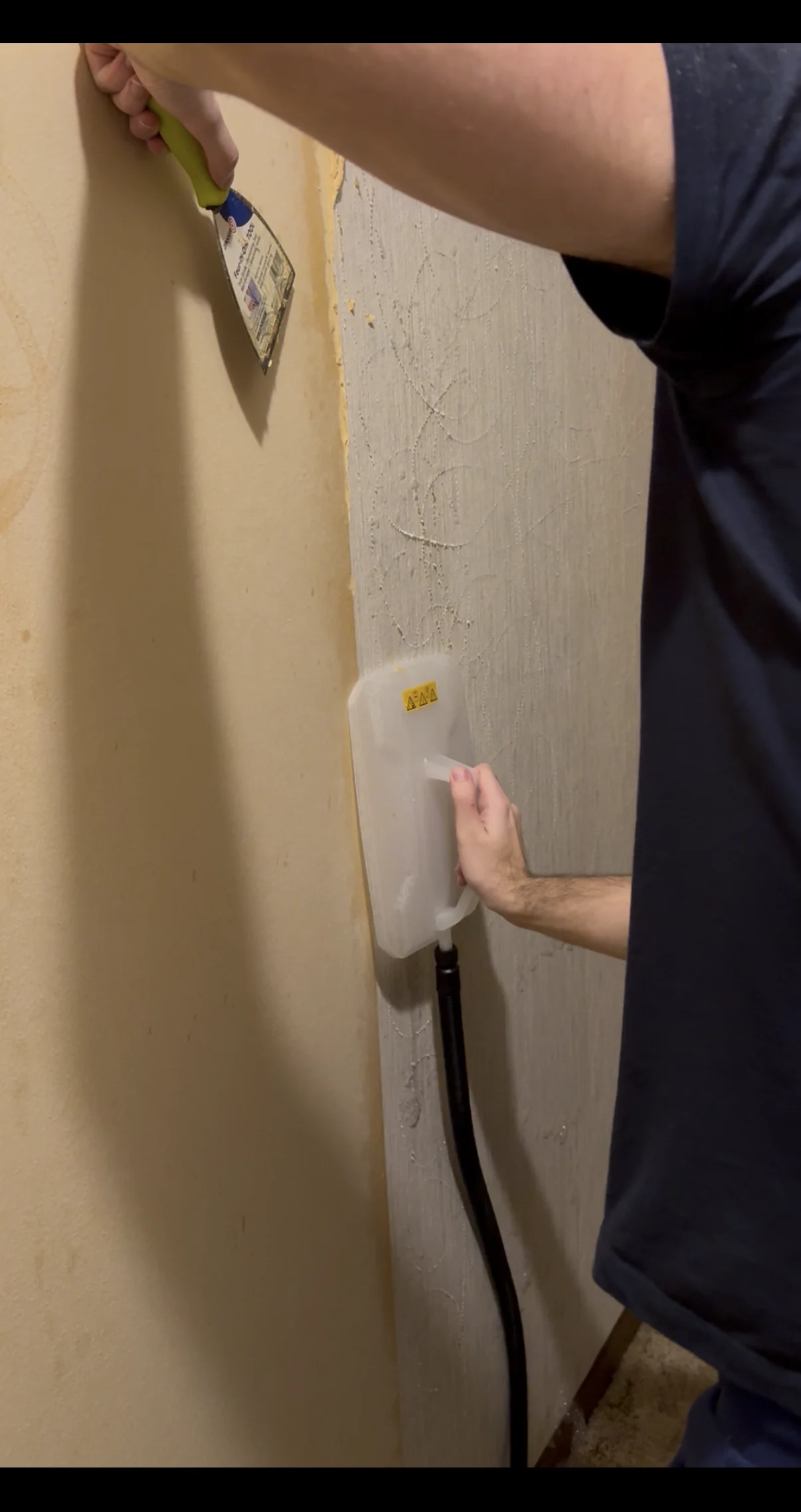 Technician steaming and lifting existing wallcovering in controlled sections beside a scraped wall