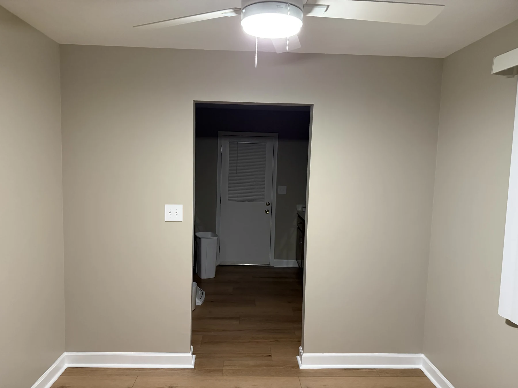 Restored interior wall after full skim coating, with a smooth continuous surface, painted baseboards, and wood flooring