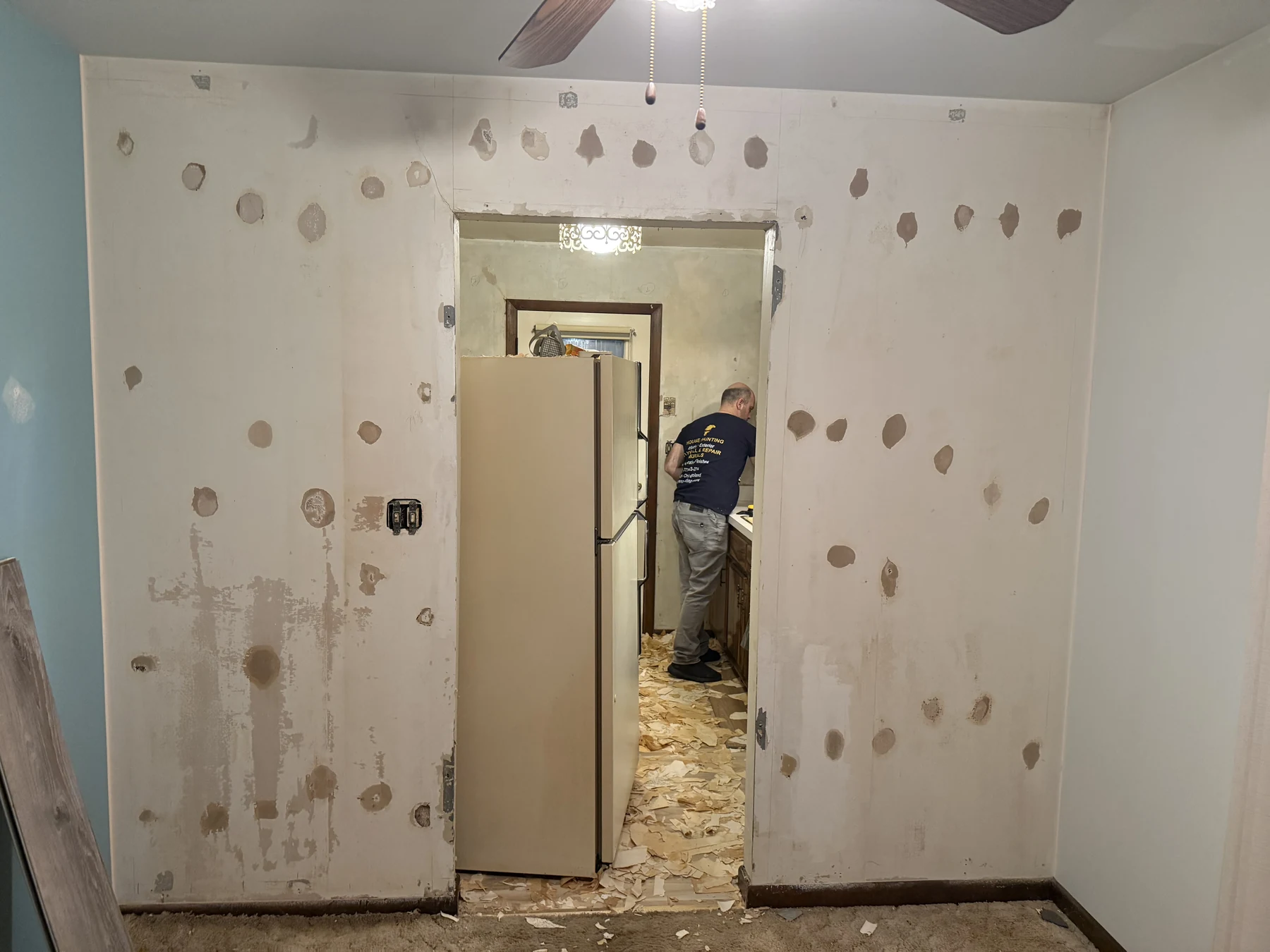 Wall after wallpaper removal with exposed adhesive residue, patch conditions, and removed wallcovering on the floor